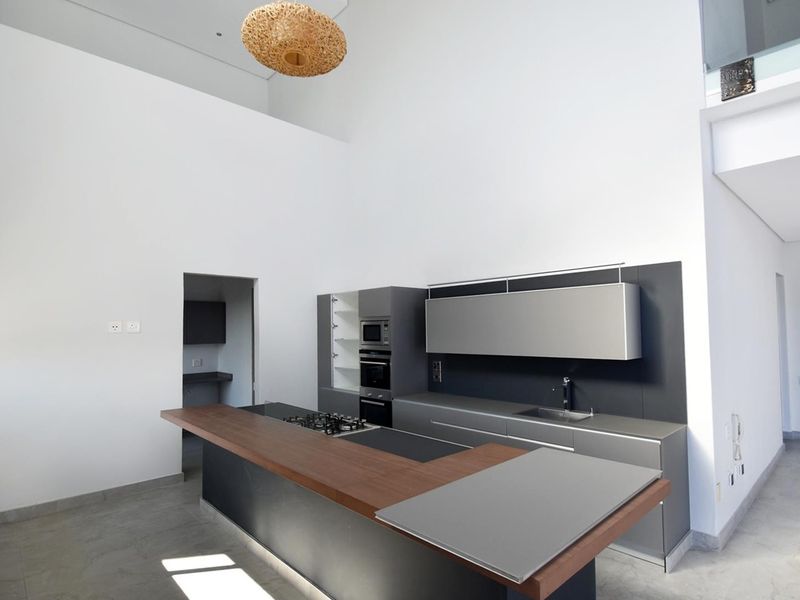 Modern kitchen featuring sleek dark cabinetry, integrated appliances, a spacious island with a wooden breakfast bar, and high ceilings in an open-plan layout.