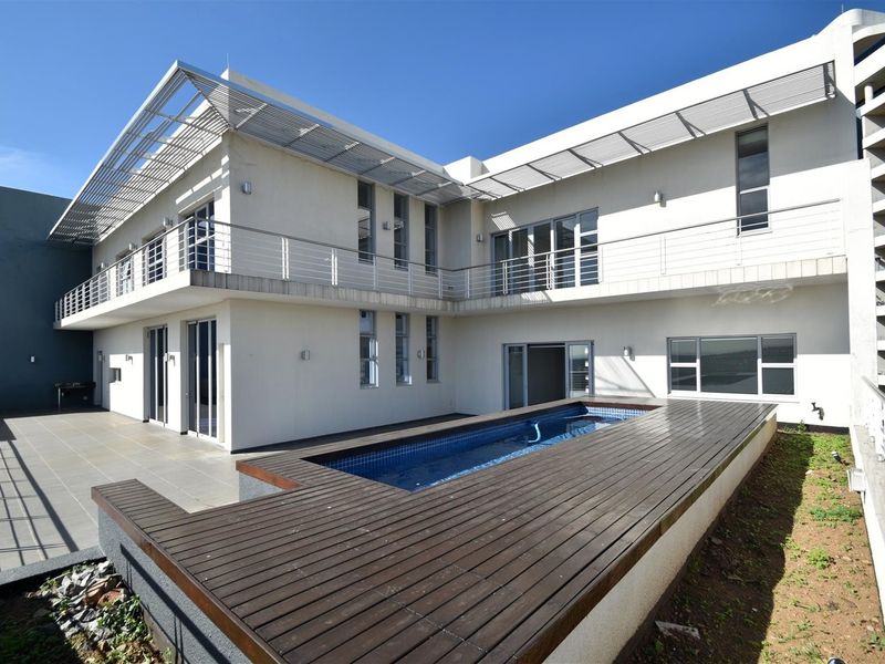 Rear exterior view of the apartment featuring a swimming pool with timber decking, a spacious balcony, and modern architectural design with sliding glass doors.
