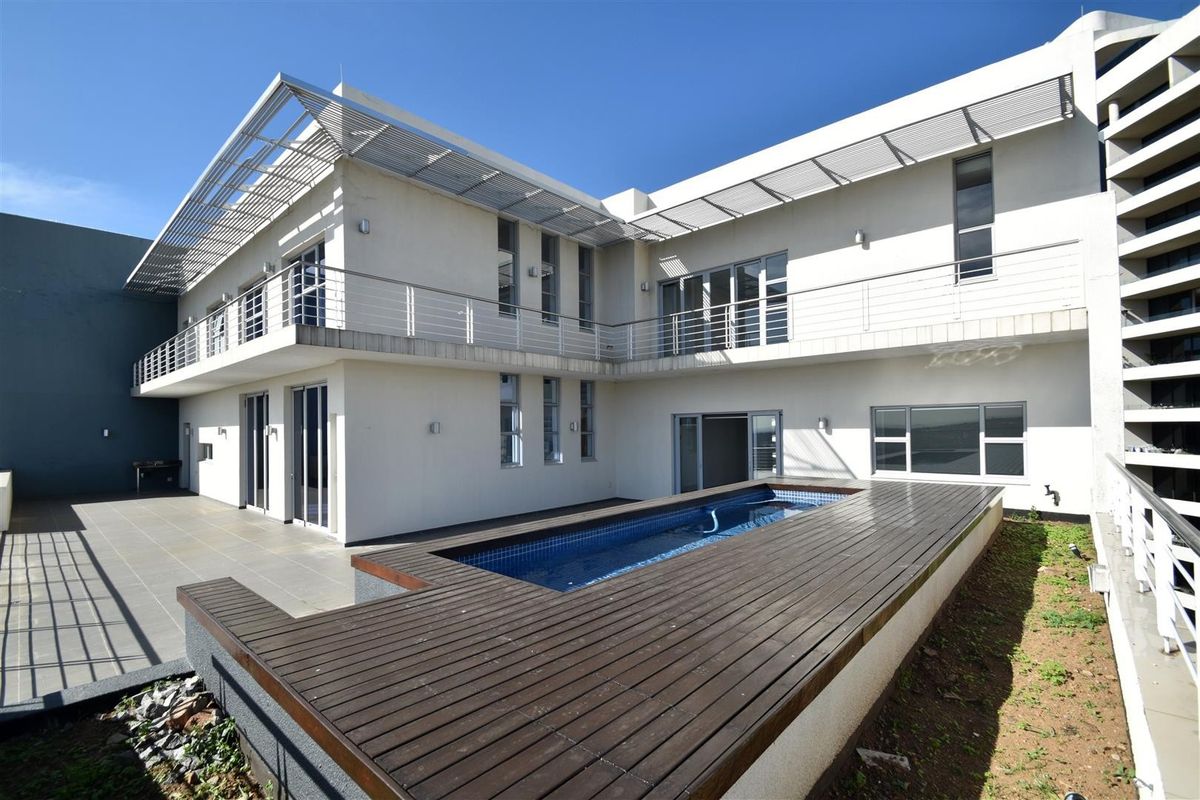 Rear exterior view of the apartment featuring a swimming pool with timber decking, a spacious balcony, and modern architectural design with sliding glass doors.