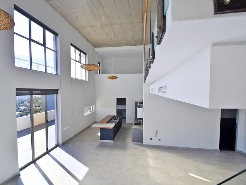 Spacious open-plan living area featuring high ceilings, modern kitchen island with integrated hob, and large sliding doors leading to a balcony.