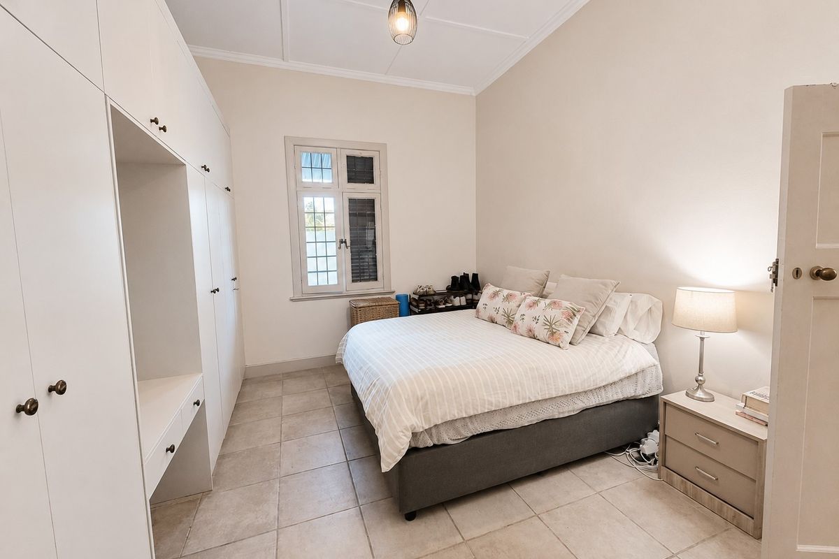 A well-maintained bedroom featuring extensive built-in cabinetry, neutral tiled flooring, and a classic casement window, offering a clean and functional living space.