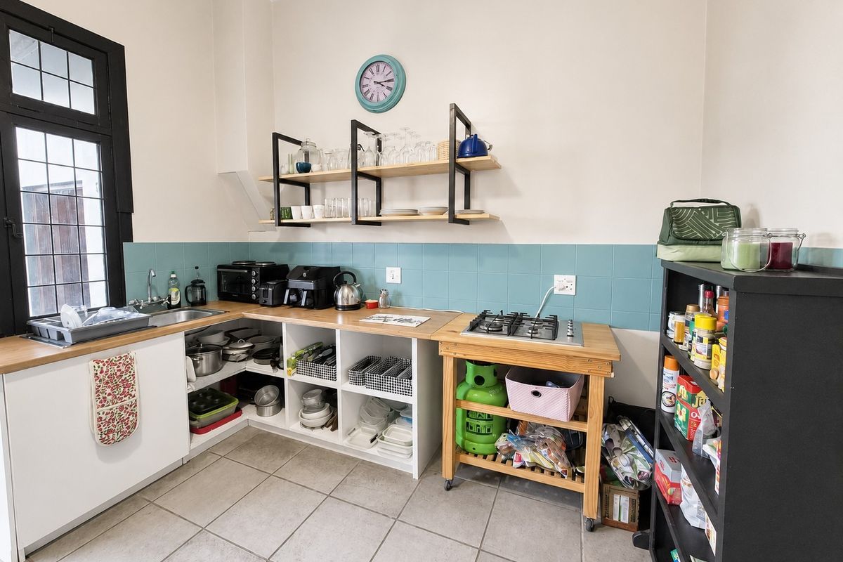 A functional kitchen area featuring a gas hob, stainless steel sink, tiled splashback, and open shelving with tiled flooring.
