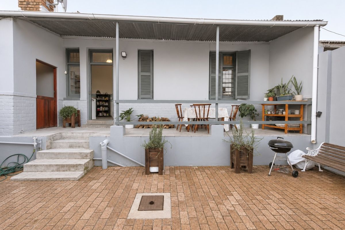A well-maintained rear exterior featuring a covered patio area with brick paving, concrete steps, and classic timber shutters on the building facade.