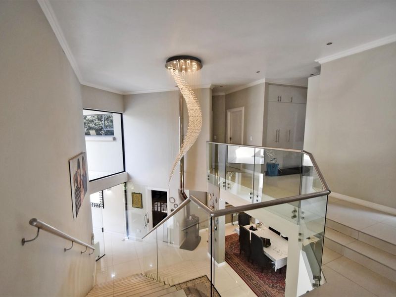 Spacious double-volume entrance hall featuring a modern staircase with glass balustrades, polished tile flooring, and a striking contemporary chandelier.