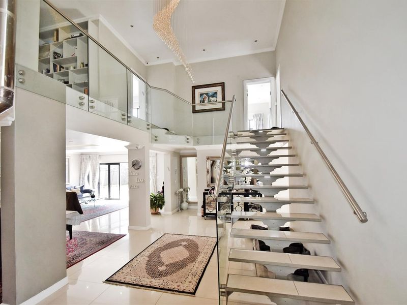 Grand double-volume entrance hall featuring a modern floating staircase with glass balustrades, polished tiled flooring, and elegant contemporary lighting.