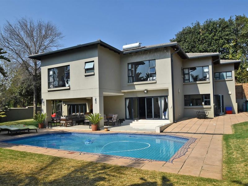 Rear view of a double-story house featuring a swimming pool, paved patio area, and large sliding doors leading into the living space.