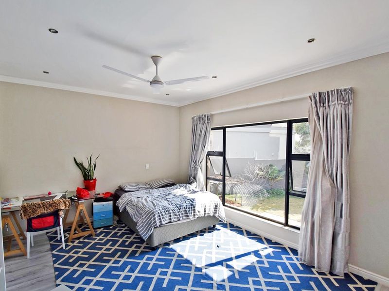 A well-lit bedroom featuring a ceiling fan, recessed lighting, and a large window overlooking the garden area.