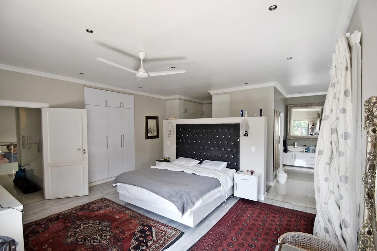 Spacious master bedroom featuring built-in cupboards, a ceiling fan, recessed lighting, and an open-plan en-suite bathroom with a vanity.