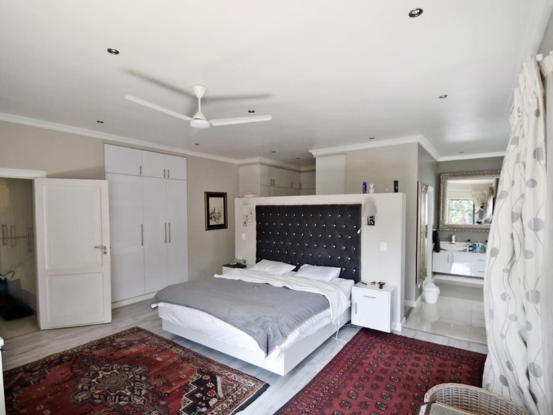 Spacious master bedroom featuring built-in cupboards, a ceiling fan, recessed lighting, and an open-plan en-suite bathroom with a vanity.