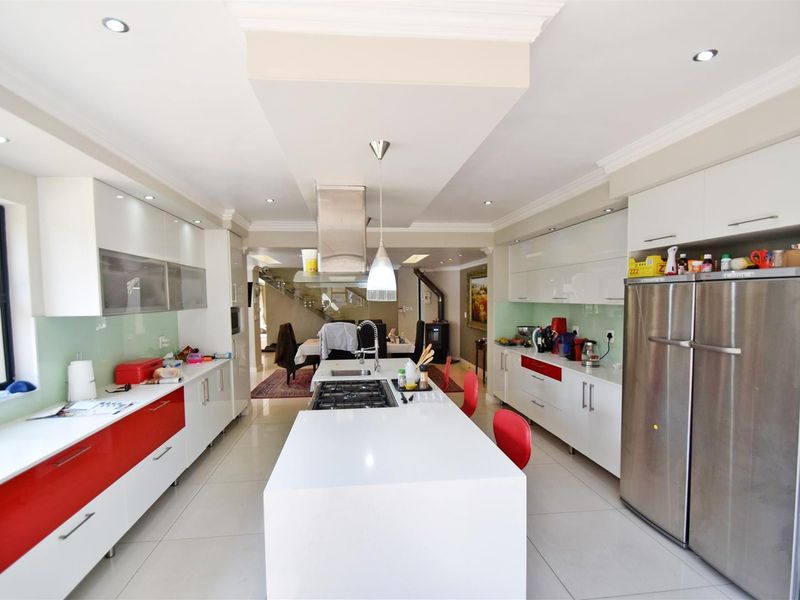 Modern kitchen featuring a central island with gas hob, sleek white cabinetry, glass splashbacks, and integrated lighting, flowing into the open-plan living area.