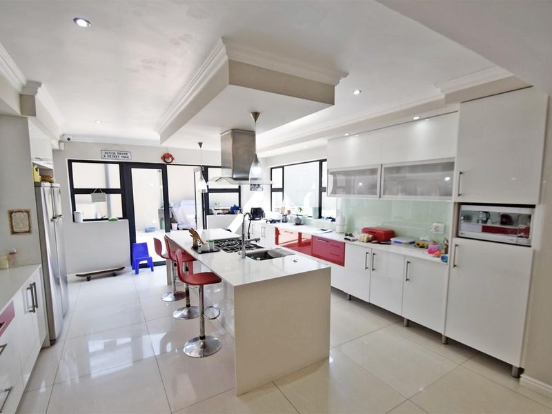 Modern kitchen featuring a central island with gas hob, integrated appliances, sleek white cabinetry, and polished tiled flooring with direct access to the patio.