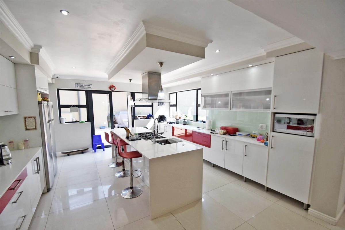 Modern kitchen featuring a central island with gas hob, integrated appliances, sleek white cabinetry, and polished tiled flooring with direct access to the patio.