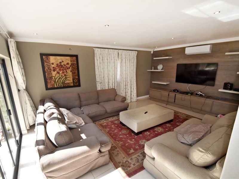 A comfortable living room featuring tiled floors, recessed lighting, a split-system air conditioner, and custom built-in media cabinetry with floating shelves.