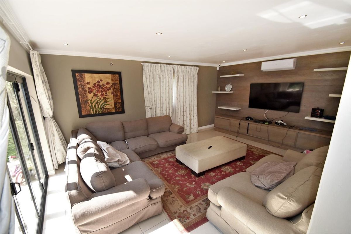 A comfortable living room featuring tiled floors, recessed lighting, a split-system air conditioner, and custom built-in media cabinetry with floating shelves.