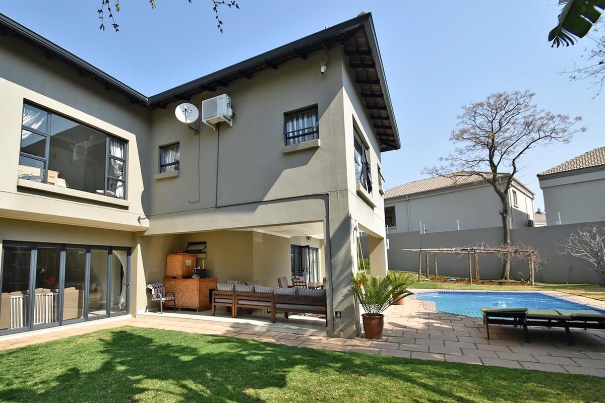 Rear view of the property featuring a covered patio, paved pool deck, and a swimming pool set within a private garden.