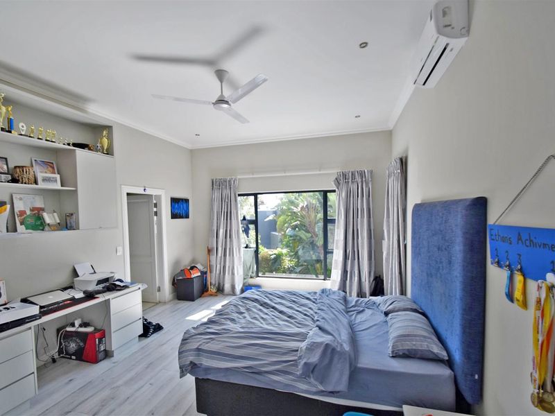 Spacious bedroom featuring laminate flooring, a built-in desk with shelving, a ceiling fan, and a wall-mounted split-system air conditioner.
