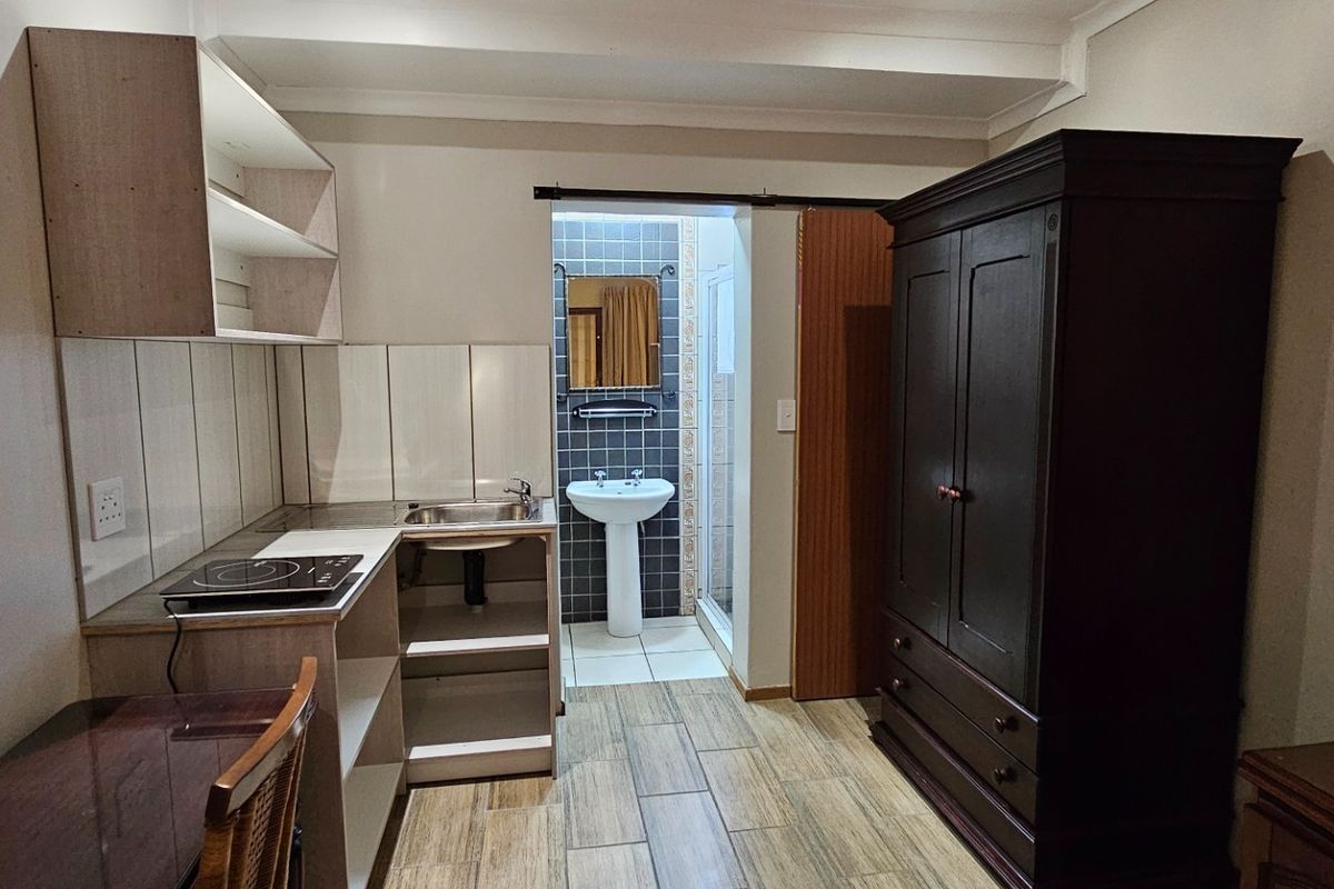 Compact open-plan studio space featuring a kitchenette with built-in cabinetry and cooktop, leading to an en-suite bathroom with a pedestal basin and shower.