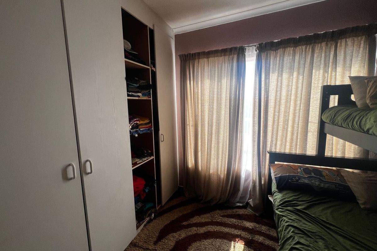 A bedroom featuring built-in wardrobes with shelving and a window with curtains, providing functional storage and natural light.