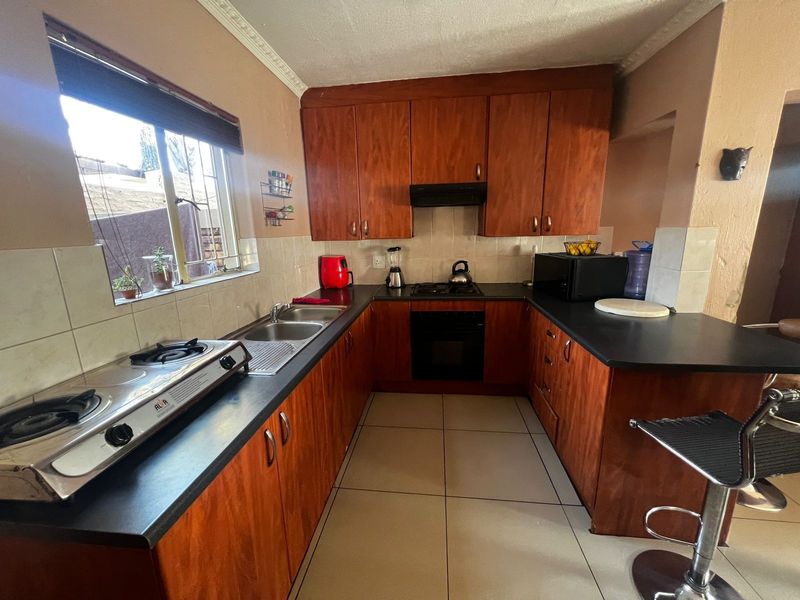 A functional U-shaped kitchen featuring wooden cabinetry, dark laminate countertops, tiled flooring, and built-in cooking appliances, offering a practical layout for daily use.