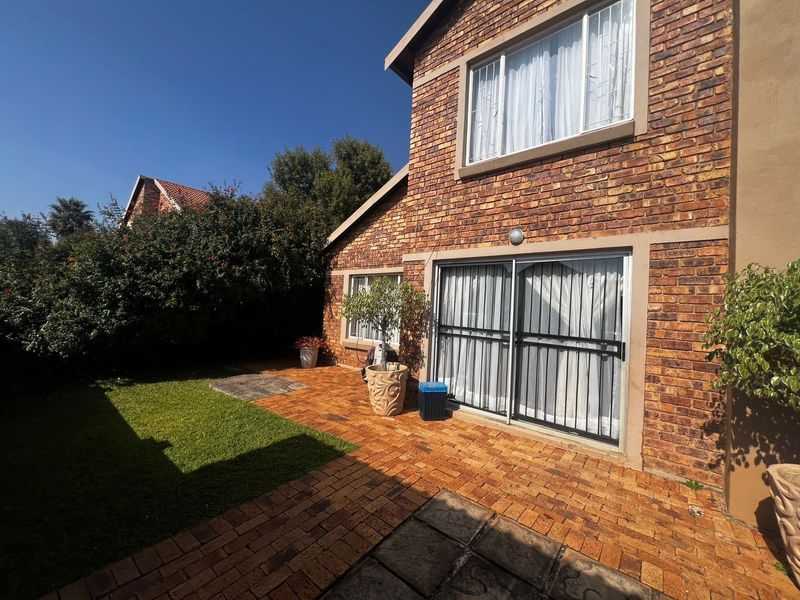 Rear view of the townhouse featuring a face brick facade, a paved patio area, and a small private garden with sliding door access.