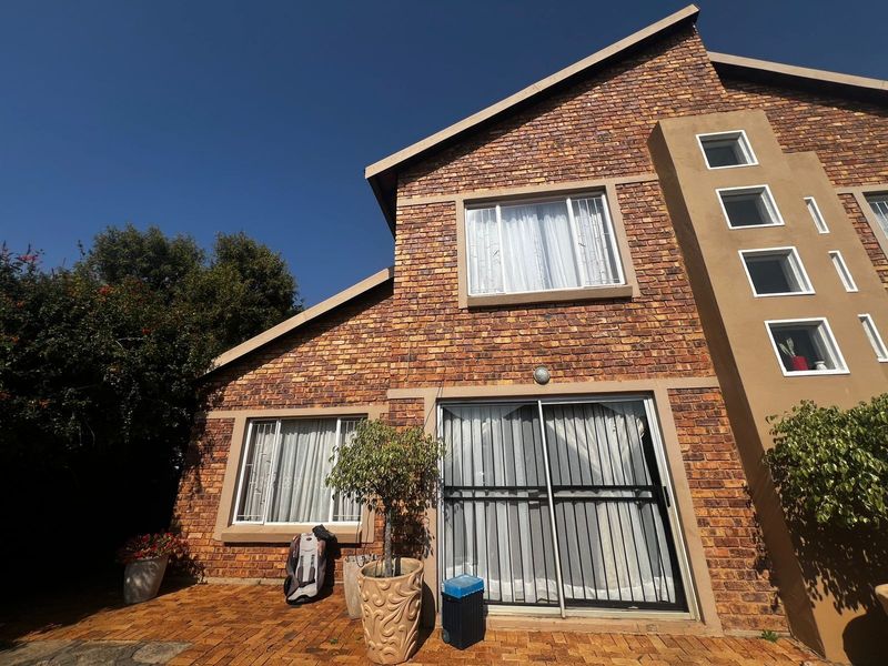 Rear elevation of a face brick townhouse featuring a paved patio area, sliding glass doors with security gates, and multiple casement windows.