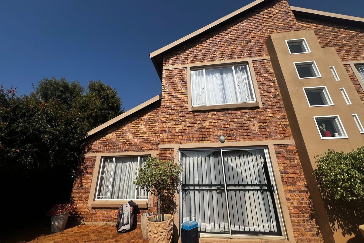 Rear elevation of a face brick townhouse featuring a paved patio area, sliding glass doors with security gates, and multiple casement windows.