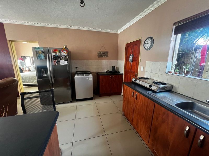 Functional kitchen featuring wooden cabinetry, tiled splashbacks, and tiled flooring, offering a practical layout with direct access to adjacent living areas.