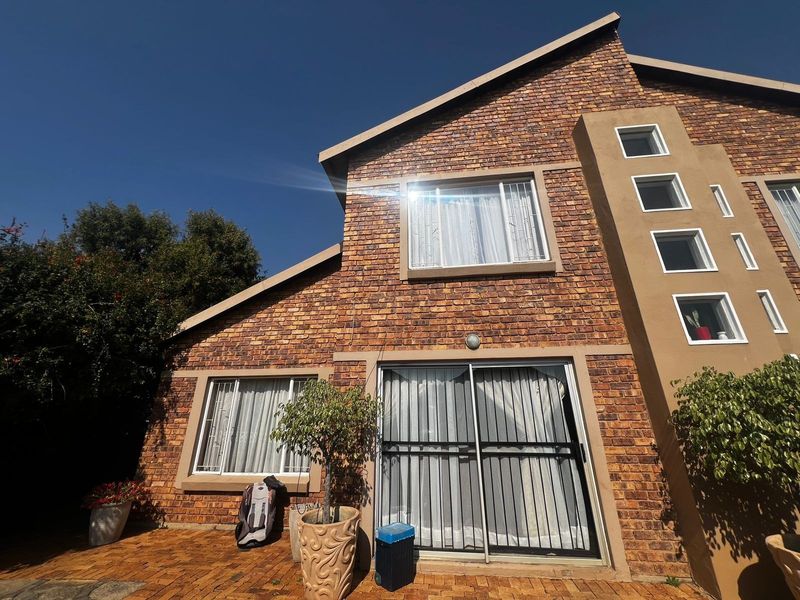 Rear exterior view of a double-story townhouse featuring face brick construction, a paved patio area, and secure sliding glass doors.