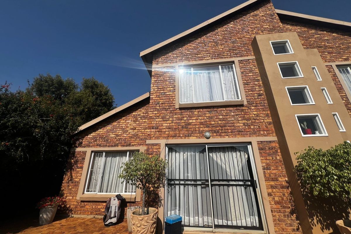 Rear exterior view of a double-story townhouse featuring face brick construction, a paved patio area, and secure sliding glass doors.