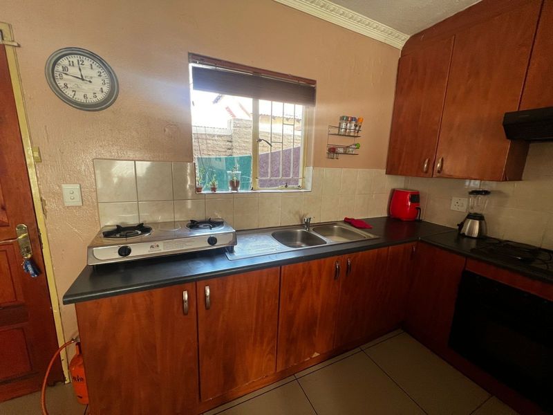 Functional kitchen featuring wood-finish cabinetry, double bowl sink, gas hob, built-in oven, and tiled splashbacks, offering a practical layout for daily meal preparation.