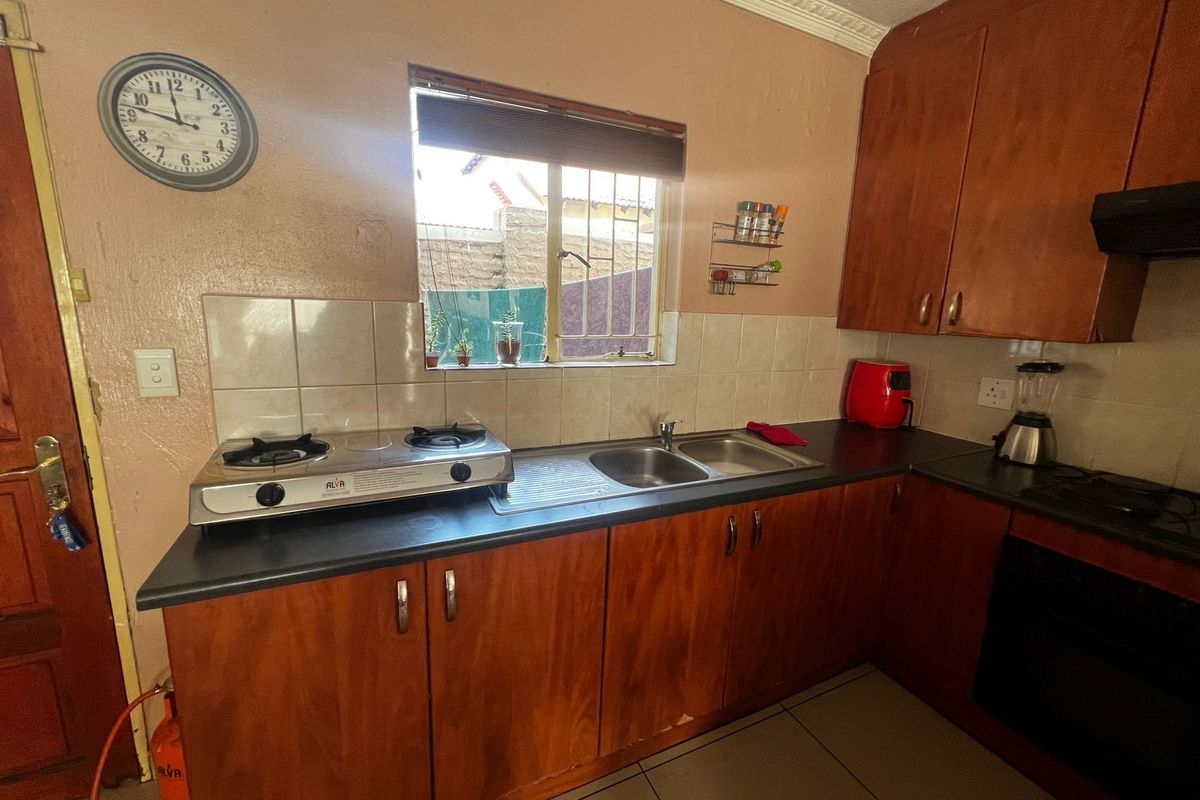 Functional kitchen featuring wood-finish cabinetry, double bowl sink, gas hob, built-in oven, and tiled splashbacks, offering a practical layout for daily meal preparation.