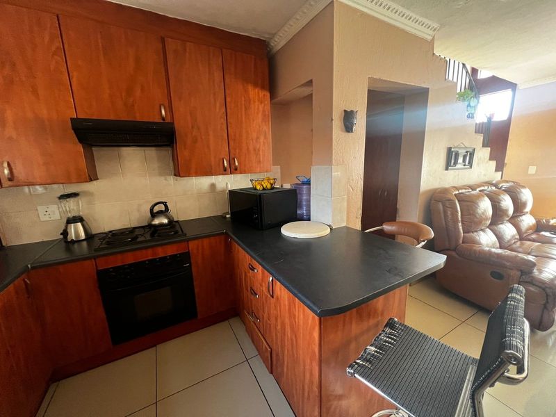Open-plan kitchen featuring wooden cabinetry, built-in oven, gas hob, and extractor fan, seamlessly flowing into the adjacent living area with tiled flooring.