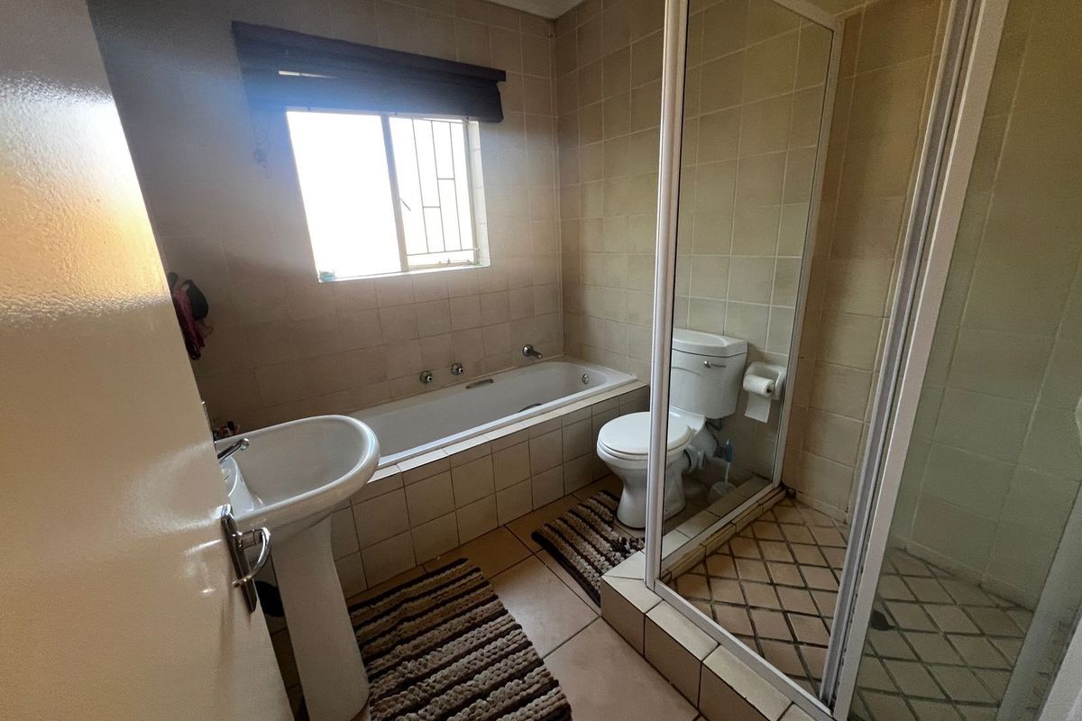 A functional bathroom featuring a pedestal basin, built-in bathtub, separate shower enclosure, and tiled finishes throughout.