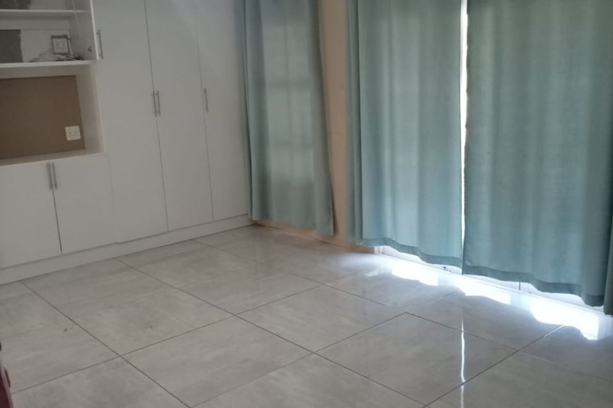 A bright, empty living area featuring large format floor tiles, built-in storage cabinetry, and a modern pendant light fixture with access to a patio.