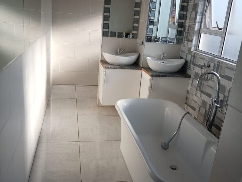Modern bathroom featuring a freestanding bathtub, dual vanity with vessel sinks, and contemporary tiled finishes.