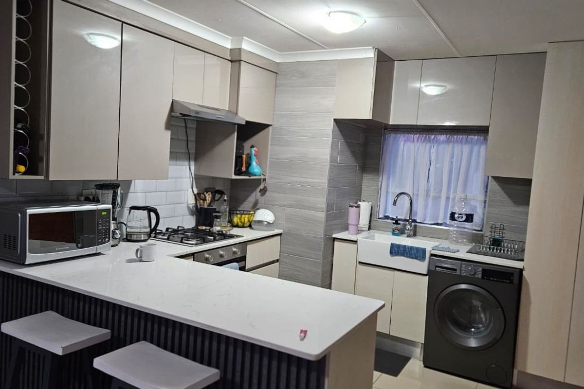 Modern kitchen featuring sleek cabinetry, quartz countertops, a breakfast bar, gas hob, and a farmhouse-style apron sink with integrated laundry appliance space.