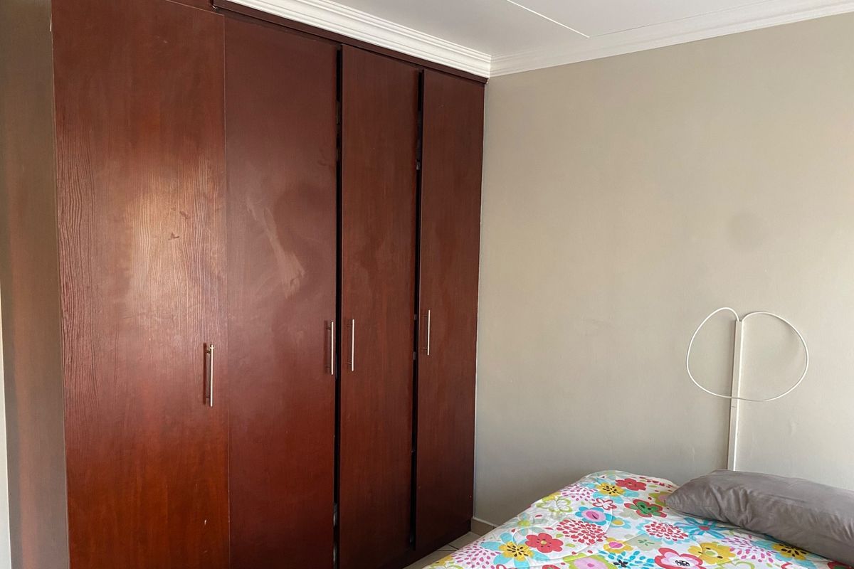 A bedroom featuring a large, dark wood-finish built-in wardrobe with modern handles and decorative ceiling cornicing.