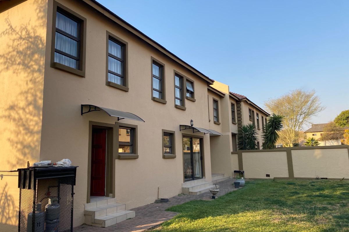Rear view of the house featuring a paved walkway, lawn, boundary wall, and access points with protective awnings.