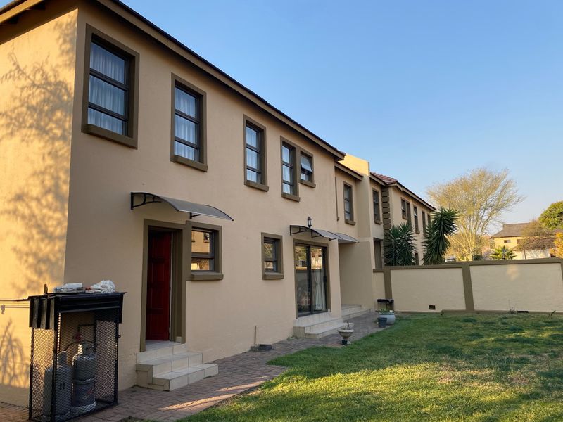 Rear view of the house featuring a paved walkway, lawn, boundary wall, and access points with protective awnings.