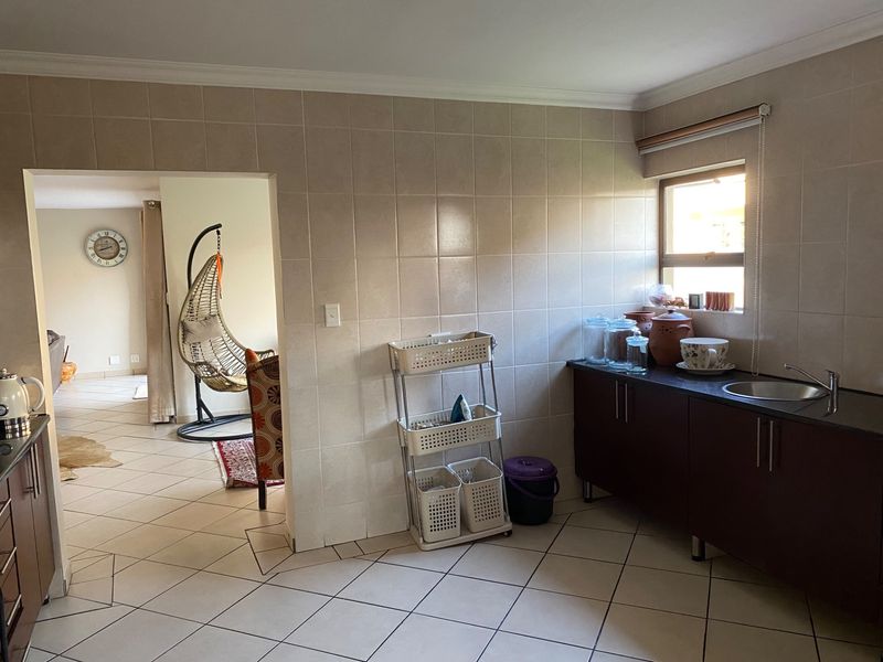 A functional scullery area featuring tiled walls, dark cabinetry, and a stainless steel sink, providing additional prep and wash-up space.