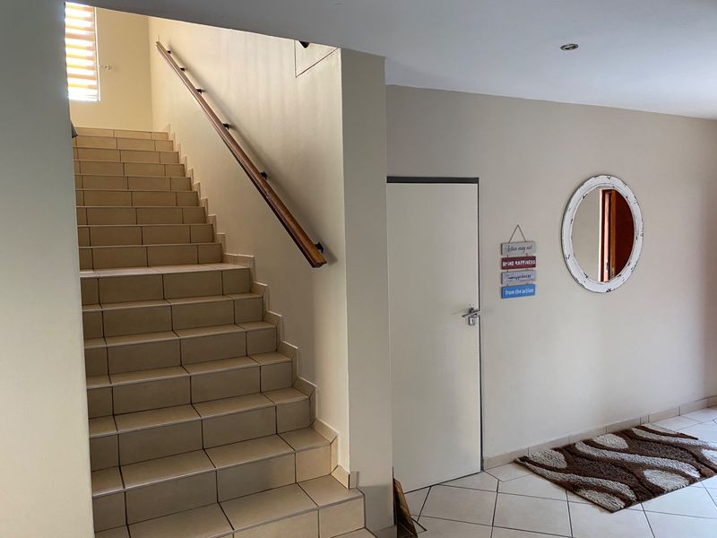 A bright entrance hall featuring a tiled staircase with a wooden handrail and neutral wall finishes, providing a clean and welcoming transition space.