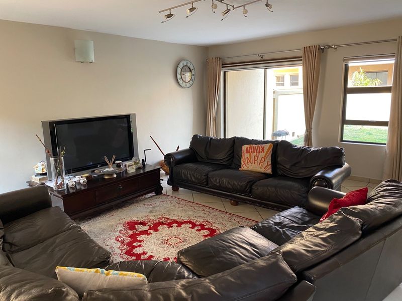 A spacious living room featuring tiled flooring, track lighting, and a large sliding glass door providing access to the rear exterior.