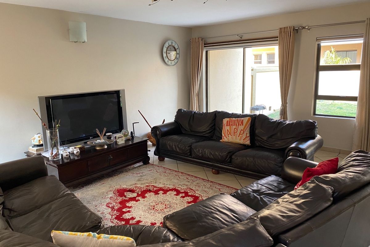 A spacious living room featuring tiled flooring, track lighting, and a large sliding glass door providing access to the rear exterior.