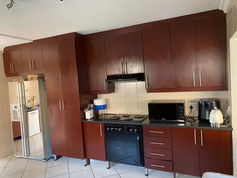 A functional kitchen featuring dark wood cabinetry, granite countertops, built-in oven, electric hob, and tiled flooring with a view into an adjacent scullery area.