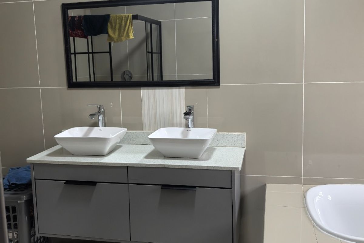 Modern bathroom featuring a double vanity with vessel sinks, wall-mounted mirror, and tiled finishes throughout.