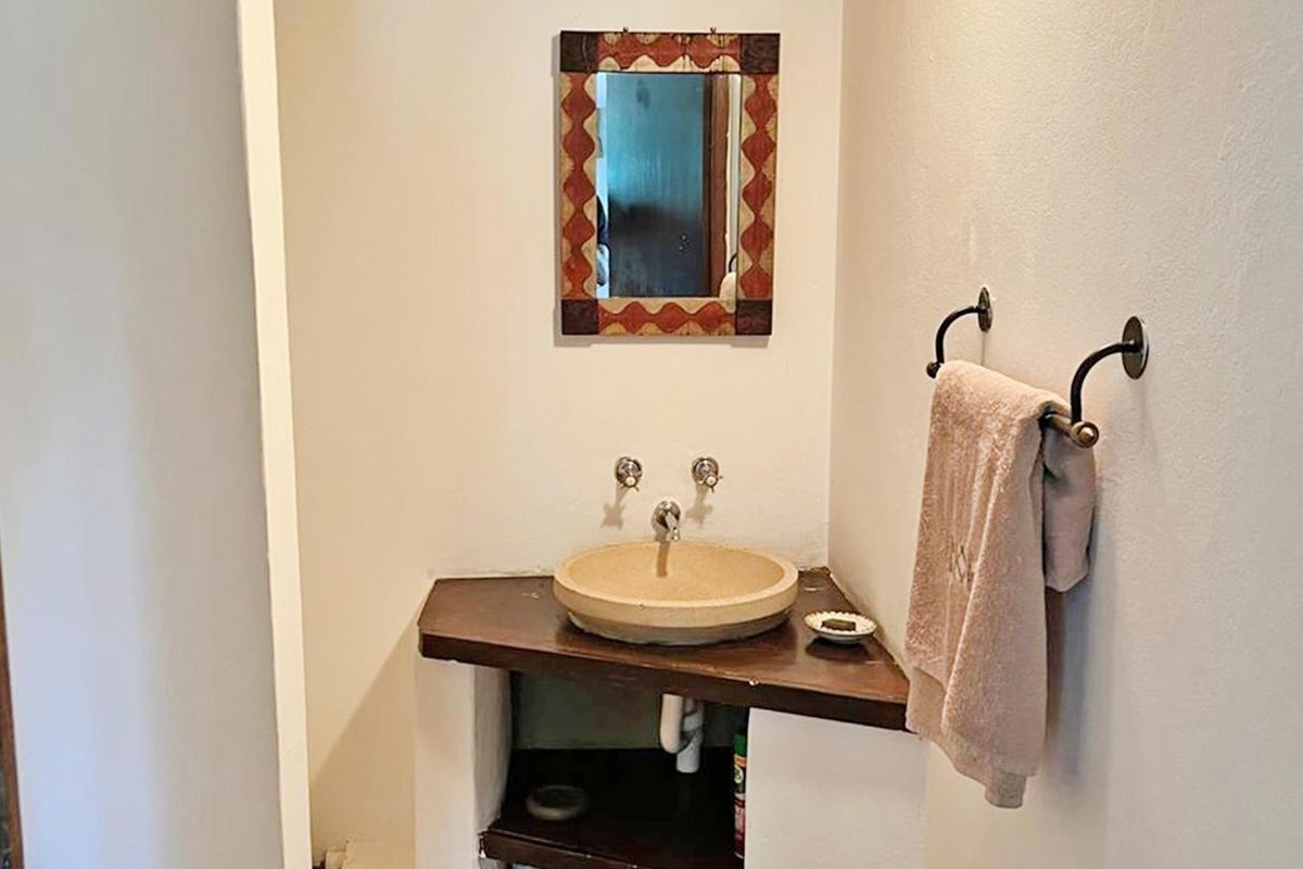 A compact bathroom featuring a stone vessel sink set on a custom wooden corner vanity with wall-mounted fixtures.