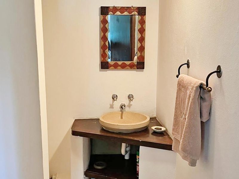 A compact bathroom featuring a stone vessel sink set on a custom wooden corner vanity with wall-mounted fixtures.