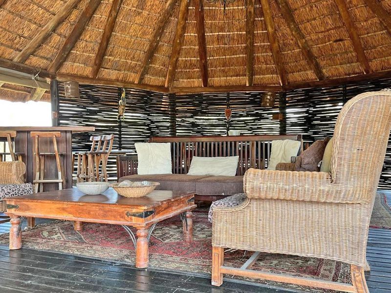 A rustic outdoor entertainment area featuring a traditional thatched roof, timber decking, and a built-in bar counter, perfect for relaxed social gatherings.