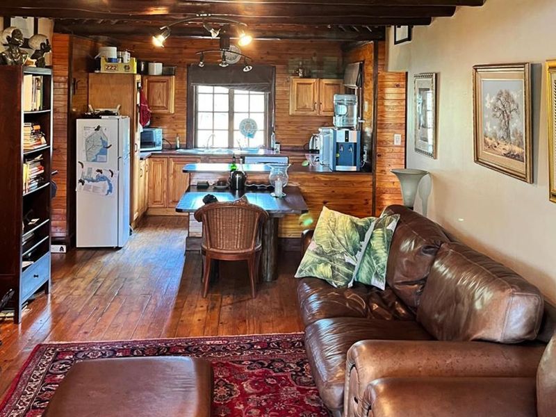 Open-plan living and kitchen area featuring rustic timber wall cladding, exposed ceiling beams, and warm wooden flooring throughout the space.