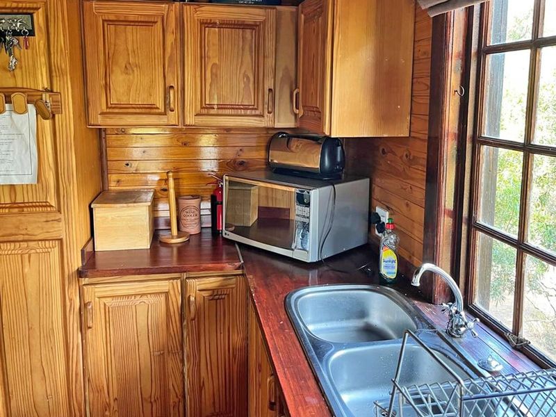 A compact kitchen featuring timber cabinetry, timber wall paneling, a double bowl stainless steel sink, and a timber countertop.